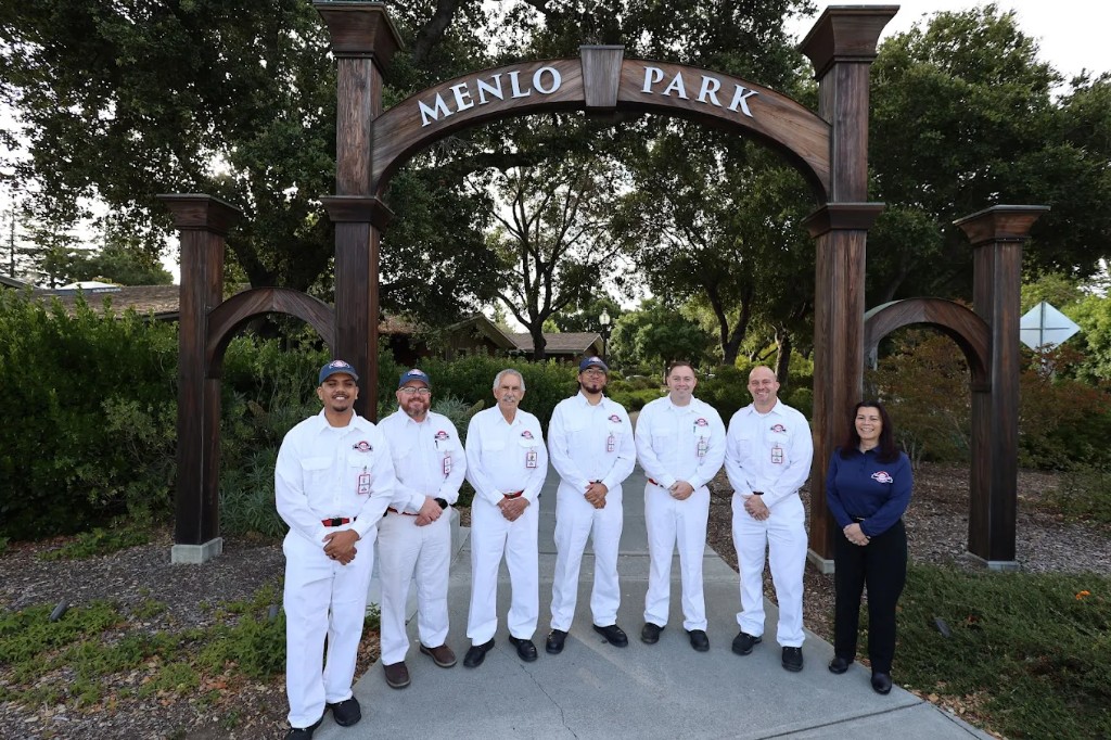 Seven Cabrillo team members in white uniforms and navy polos standing beneath the Menlo Park welcome arch on the Peninsula.