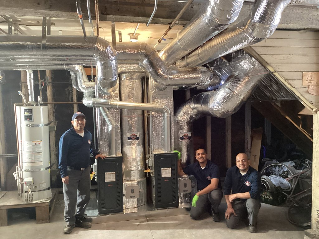 Three Cabrillo HVAC technicians beside two newly installed Trane furnaces, insulated ductwork and a residential water heater in a customer's San Francisco basement.
