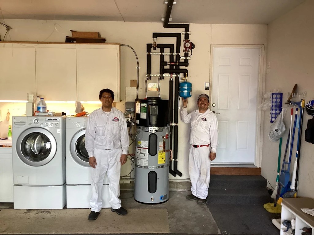 Two Cabrillo plumbers beside a newly installed water heater and expansion tank in a customer's garage utility area.